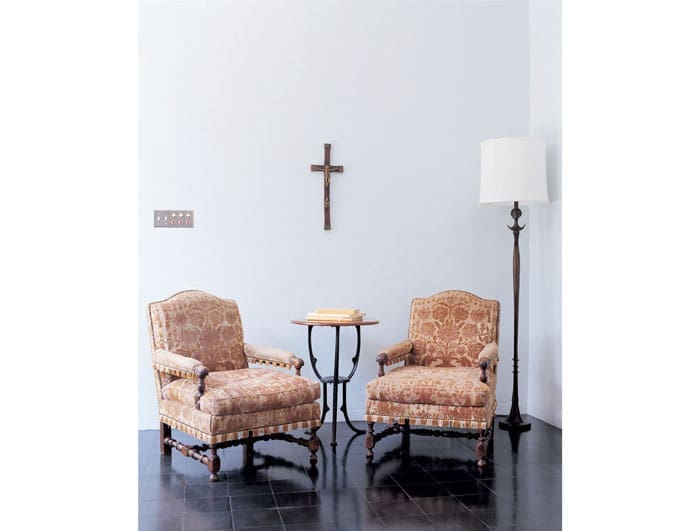 A pair of timeworn 18th-century Italian walnut open arm chairs, covered in cut velvet, flanks a round pedestal table 