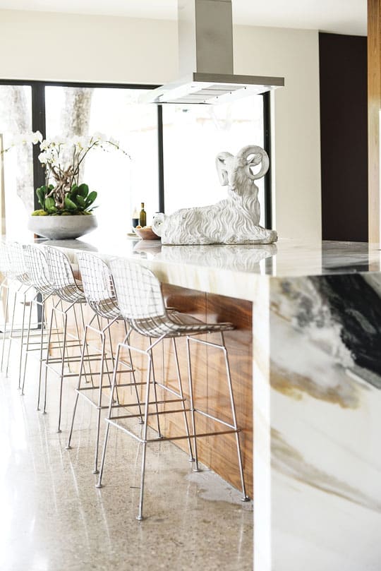 Bordering the kitchen is a Calacatta marble counter, juxtaposed with walnut. Ceramic ram sculpture found at an estate sale. Knoll Bertoia bar stools marry white leather with stainless steel.