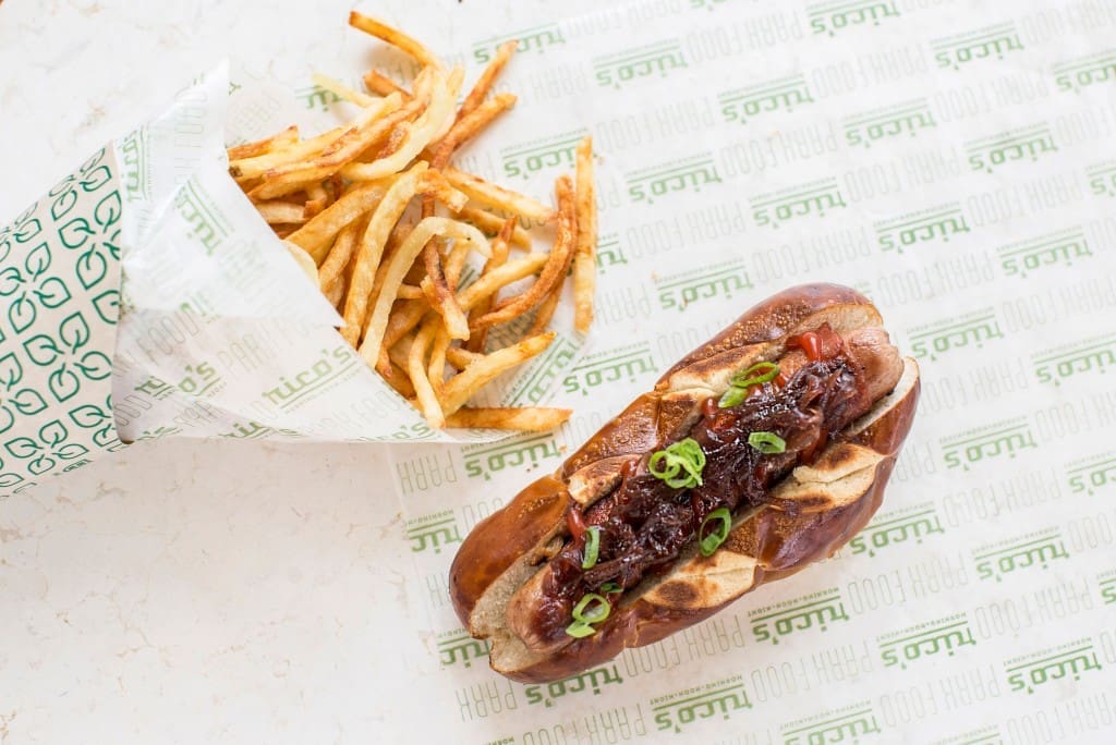 Rico's H-Town Dog — bacon-wrapped all-beef hot dog on a pretzel bun served with onion jam and ketchup.