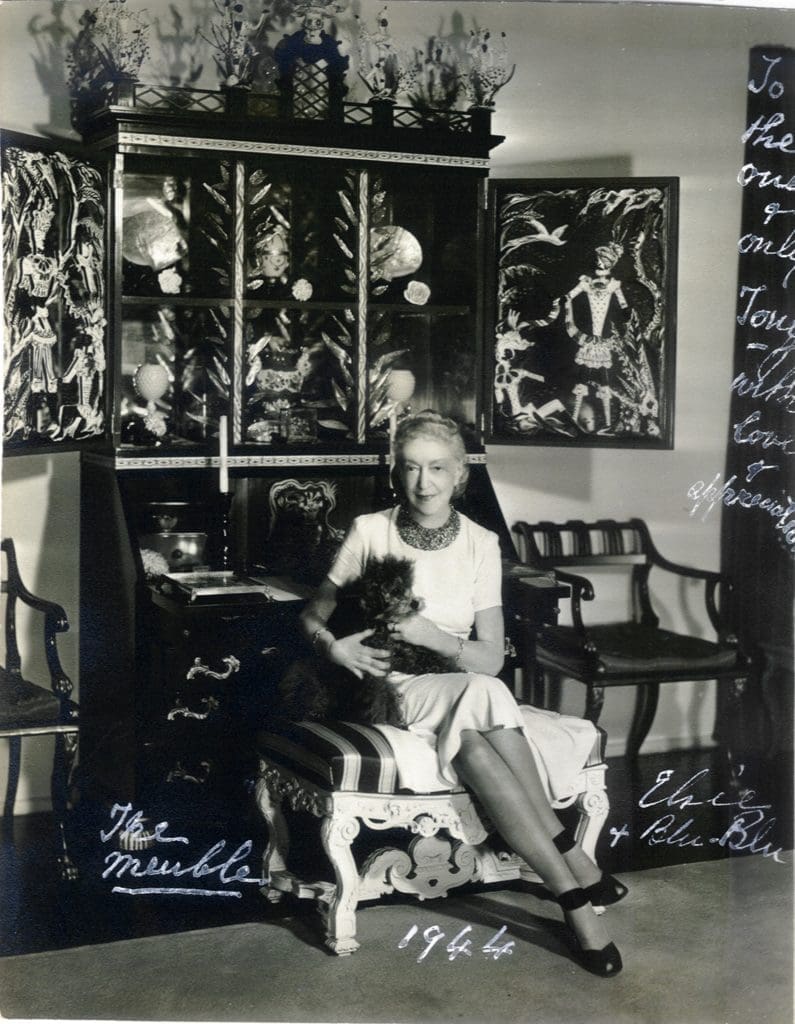 Elsie de Wolfe with Blu-Blu in front
of her meuble designed by Tony
Duquette, 1942
