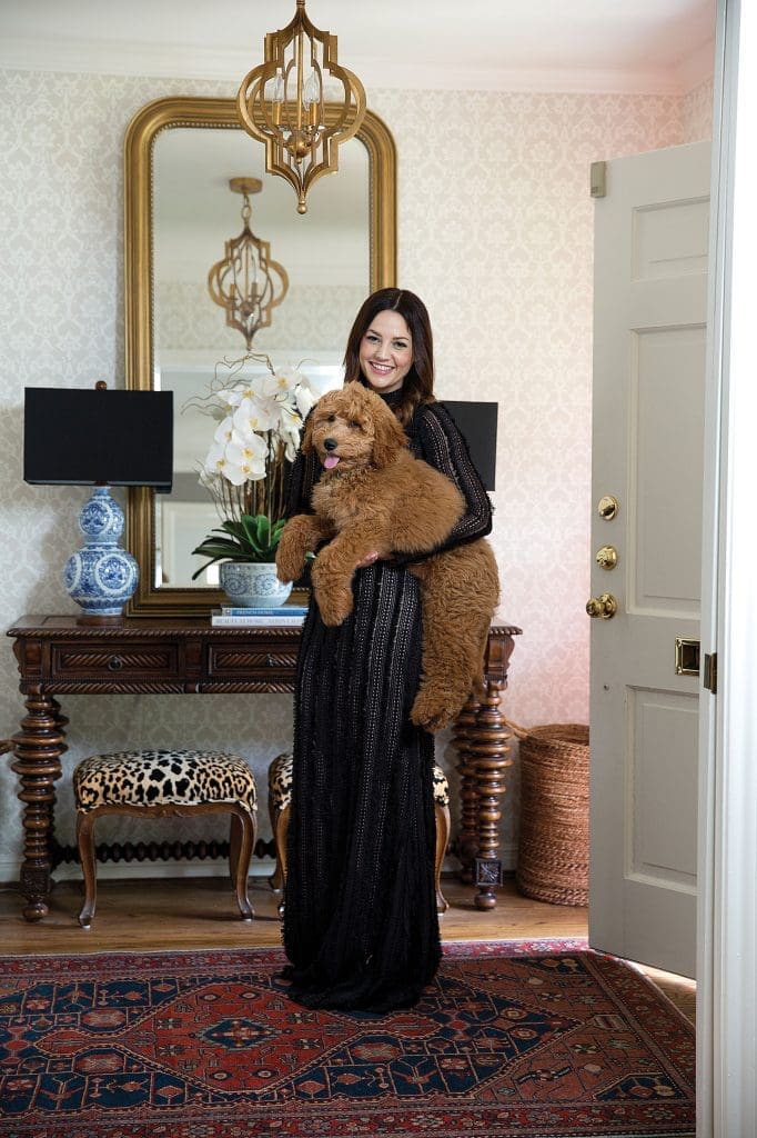 Caroline Harper Knapp in a dress by Hunter Bell, with goldendoodle Rosie. Farrow & Ball wallpaper. Ralph Lauren lamps. Pendant light by Regina Andrew Design. Vintage benches reupholstered in Jamil Natural by Calico Corners.