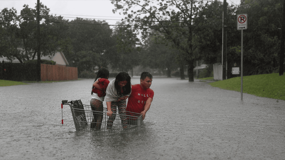 Good samaritan helps children cross flooded street with the help of a grocery basket. (Photo by Joe Raedle / Getty Images) 