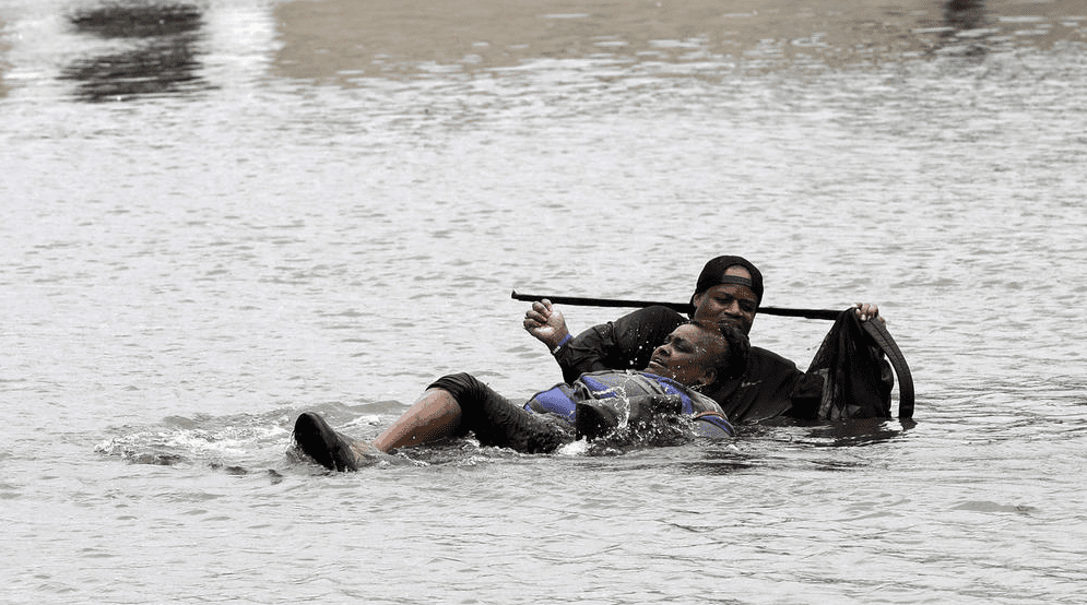Man helps push woman to safety in rising flood waters. 