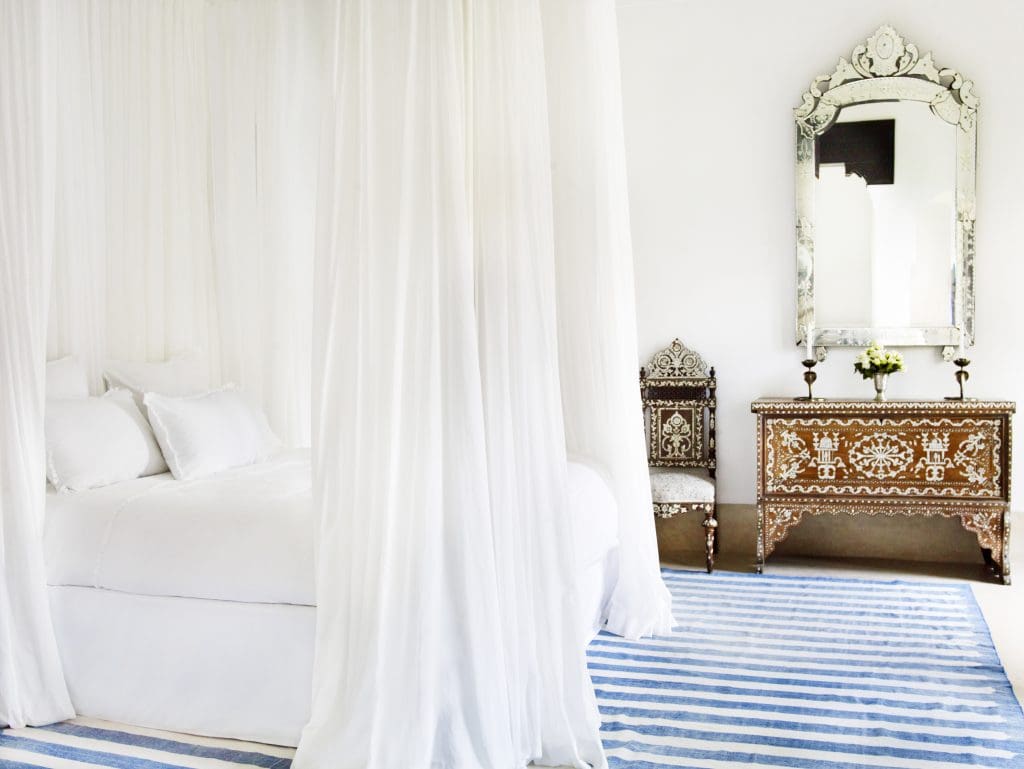 A blue striped rug, mother-of-pearl-inlaid dresser, and crisp white bed create perfection in the Tangier Suite