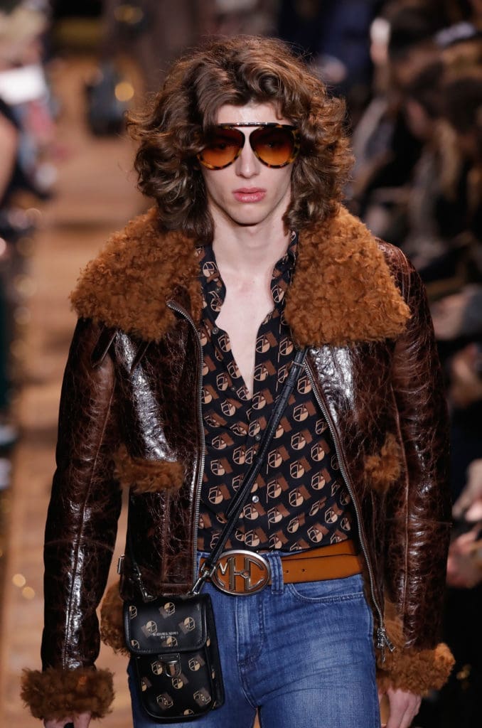 A model channels the '70s in a Michael Kors leather jacket with shearling trim, print nik nik shirt,  denim jeans, belt with big buckle, and cross-body bag. (Photo by JP Yim/Getty Images for Michael Kors)