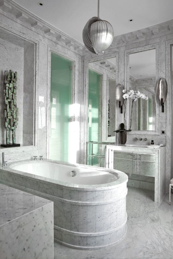 In an Avenue d'Eylau apartment, Carrara marble walls and floors detailed by Deniot with faux marbre moldings; Verner Panton 1960s "Moon" light fixture. Herve Van der Straeten wall sconces in silver leaf. 