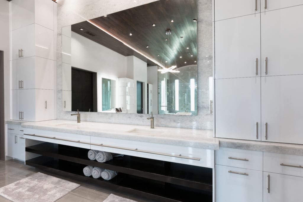 Double vanities with quartzite countertops are flanked by  white gloss frameless cabinets in the Frankel Building Group home.