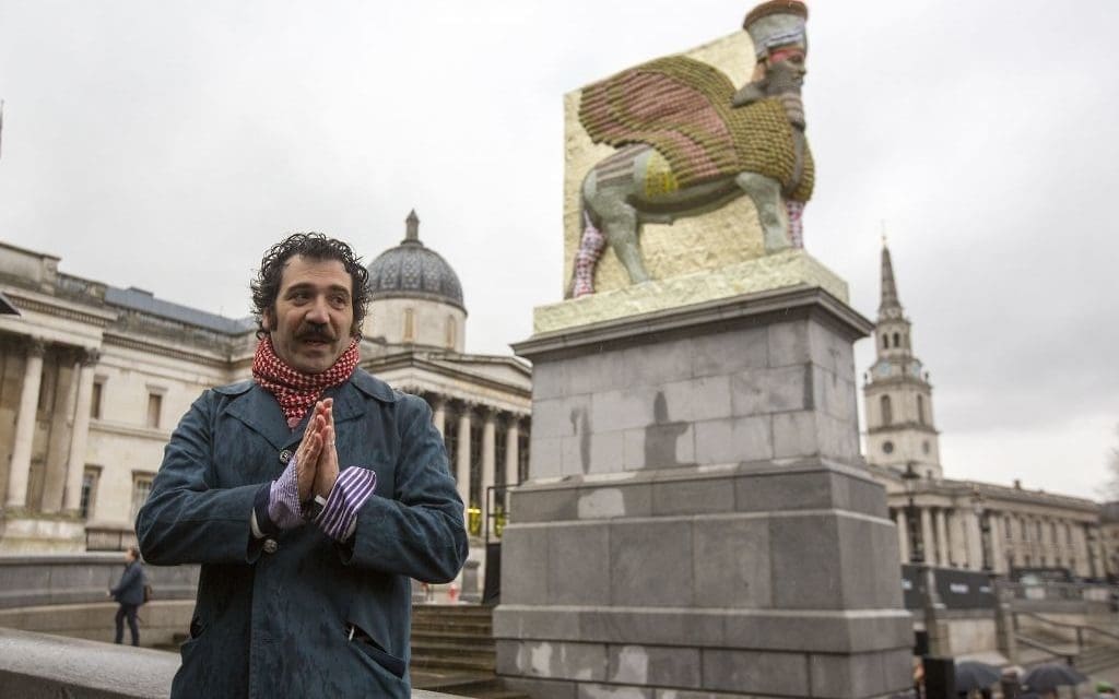 Michael Rakowitz stands with his work in London's Trafalgar Square, 2018, "The Invisible Enemy Should Not Exist." The human-headed figure of a winged bull (lamassu) is constructed from cans of Iraqi date-syrup, a staple of the region's cuisine. (Photo Rick Findler/PA Wire, courtesy Jewish News Times of Israel)