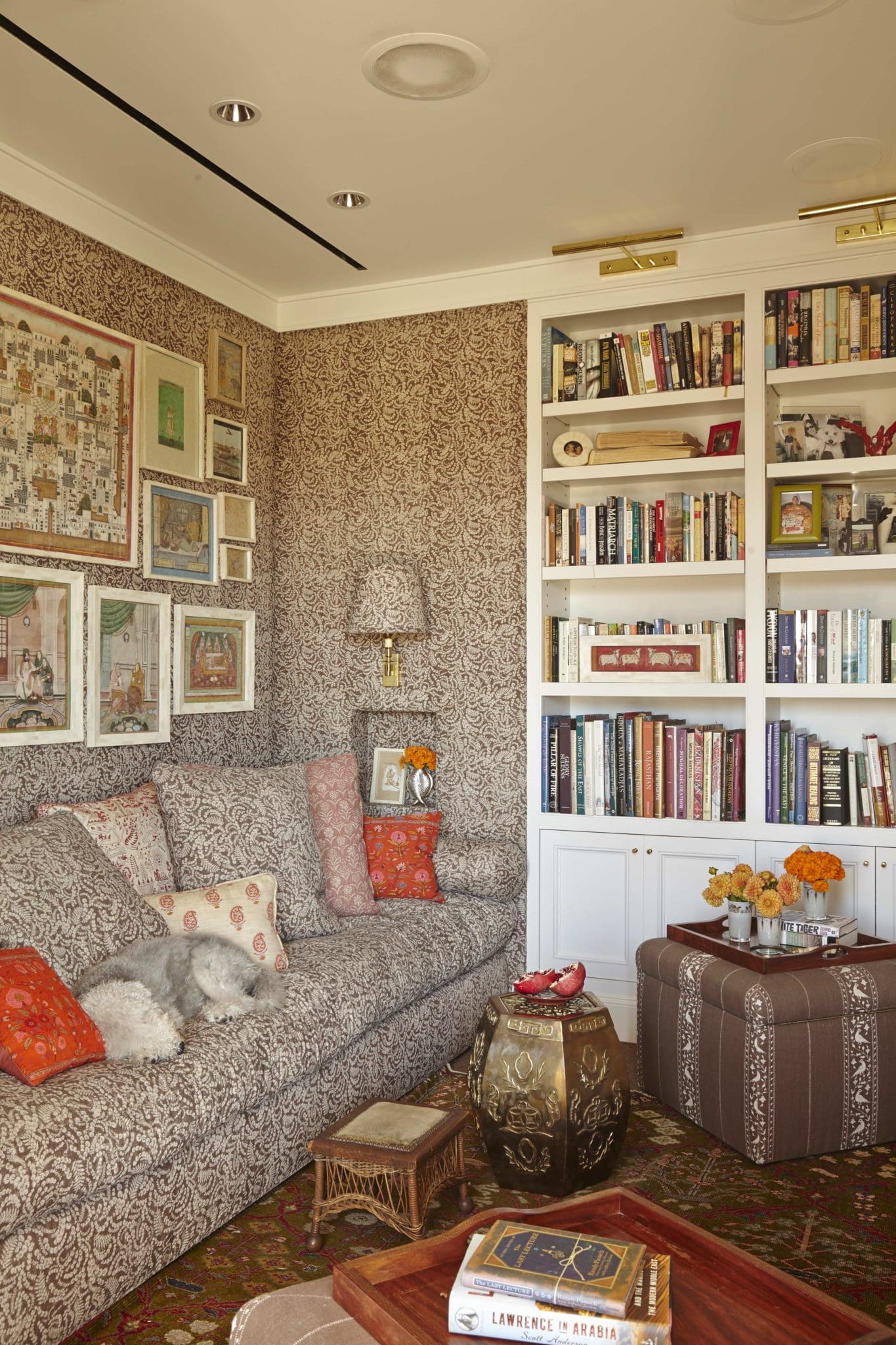 In the TV room, Fine's collection of Indian miniatures and portraits framed in camel bone, discovered in New Delhi. Lisa Fine Textiles Malula covers the walls, sofa, and sconce shade. GoGo, a Bedlington terrier, sleeps on the sofa. the agra rug from Abrash Rug Gallery. ceramic stool from Ceylon et Cie.