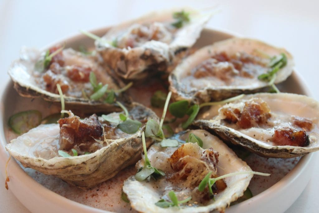 Grilled oysters served with garlic, Parmesan, and guanciale pork. Photo by Brittany Baerwald.