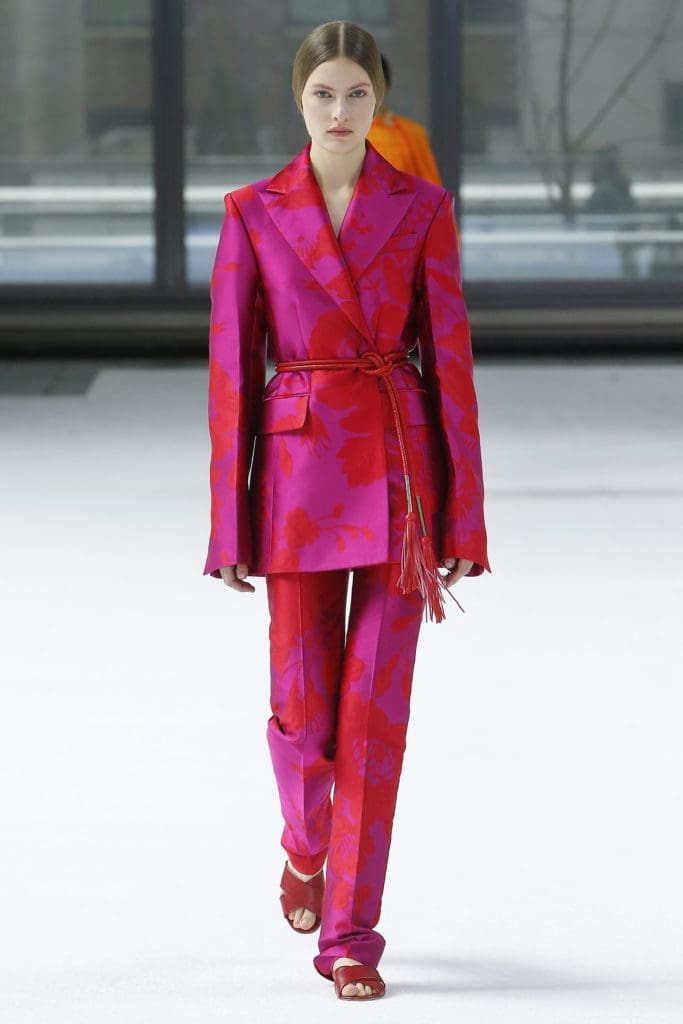 Carolina fuchsia floral jacquard notched lapel one-button jacket and straight leg pant, imperial red tubular belt, red flat sandals. (Photo courtesy of Carolina Herrera)