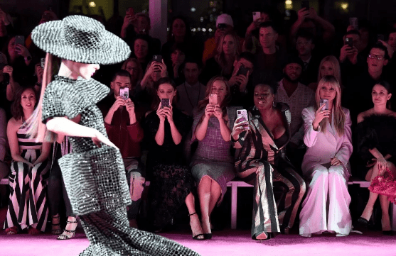 Leslie Jones, in striped pantsuit, and Heidi Klum, in white flared trousers and jacket, capture the Christian Siriano runway show on their cell phones. (Dimitrios Kambouris/Getty Images for NYFW: The Shows)