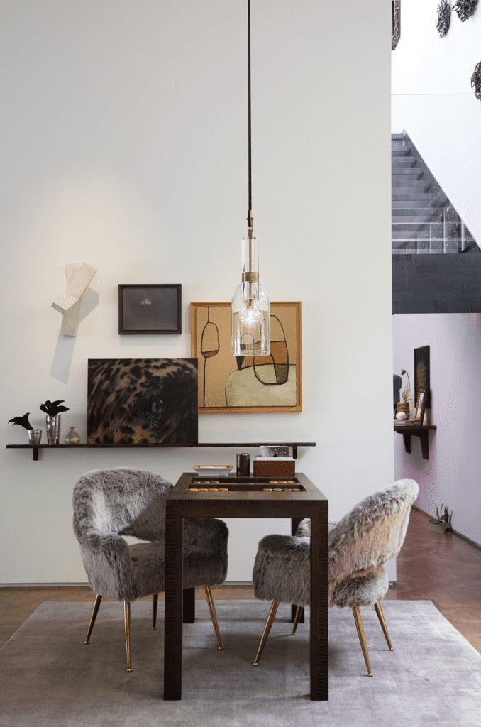 Brian Bolke and Faisal Halum. Interior Design Gonzalo Bueno, published September 2017. Photographed by Lisa Petrole. In the living area of Brian Bolke and Faisal Halum's  1987 Lionel Morrison-designed home, lizard-embossed Karl Springer backgammon table. Holly Hunt pendant light. French 1950s chairs. Wall sculpture Garth Evans’ "Canal No. 15," 1982; Tom LaDuke’s "Bruegel, Phantom," 2013; Alexis Fraikin’s "Untitled," 2002; Hope Atherton’s "Untitled," 2002. Far right, on floor, Tony Matelli’s "Weed #314" sculpture, 2014. 