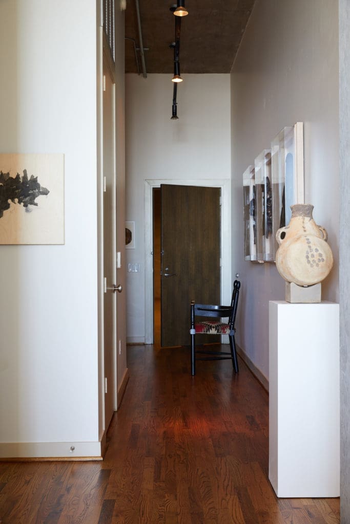 In the hallway, large red-clay pottery piece from Area. Antique chair upholstered in a Navajo rug was bought at auction in Dallas. Custom spotlights illuminate framed African relics on wall. (Photo by Pär Bengtsson)