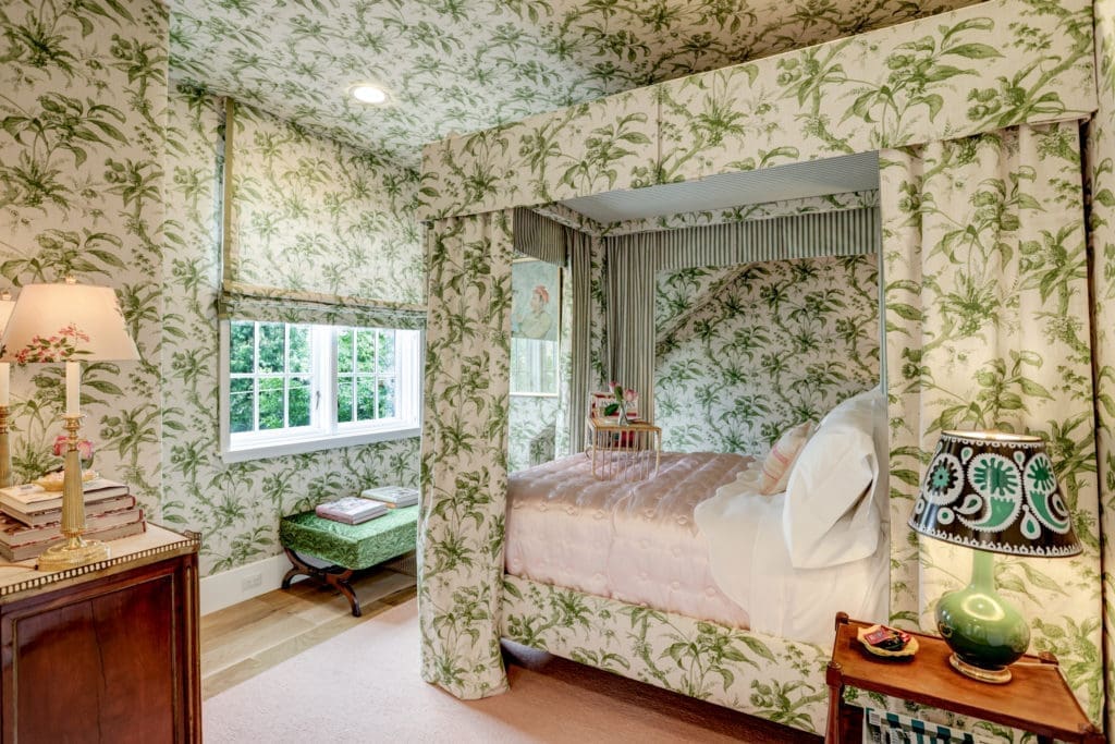 This secondary bedroom, designed by Lisa Fine, features upholstered walls, large closet, hardwood floors, built in bookcase, and ensuite bath.