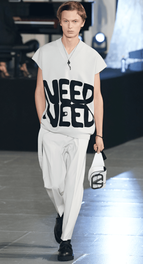 Might we suggest looking ever the man in the know via a tunic-like top emblazoned with "Need Need," paired with a gender fluid cross-body bag.