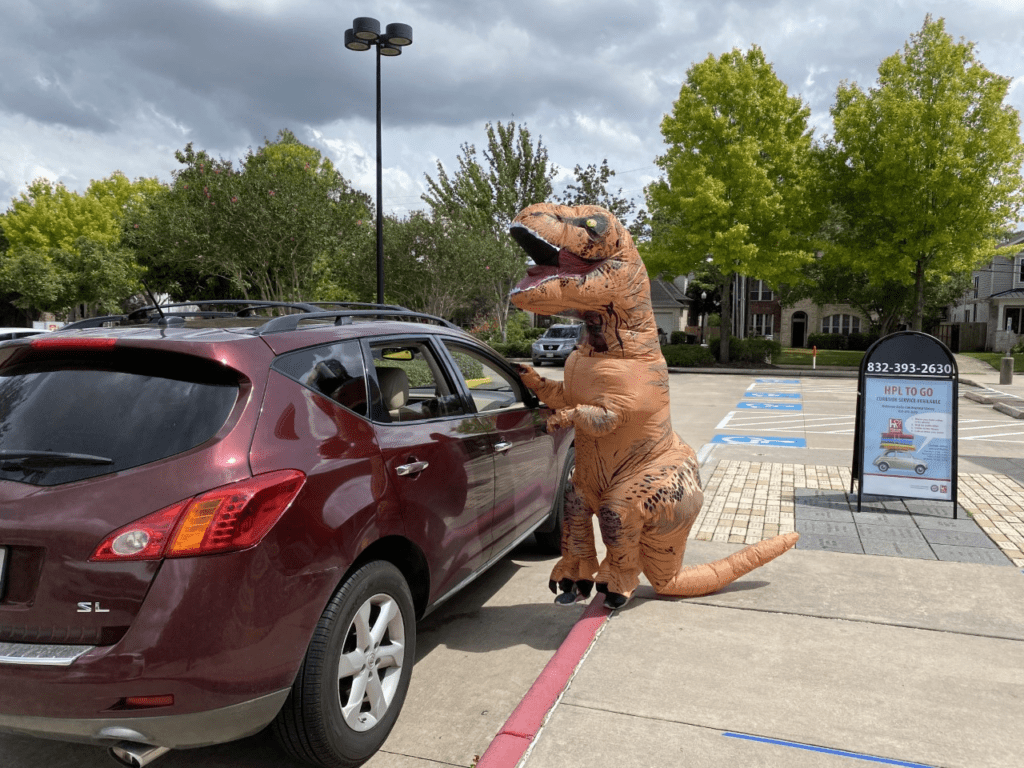 Rory the Dinosaur encourages kids to keep reading during the pandemic with HPO TO GO curbside pickup.