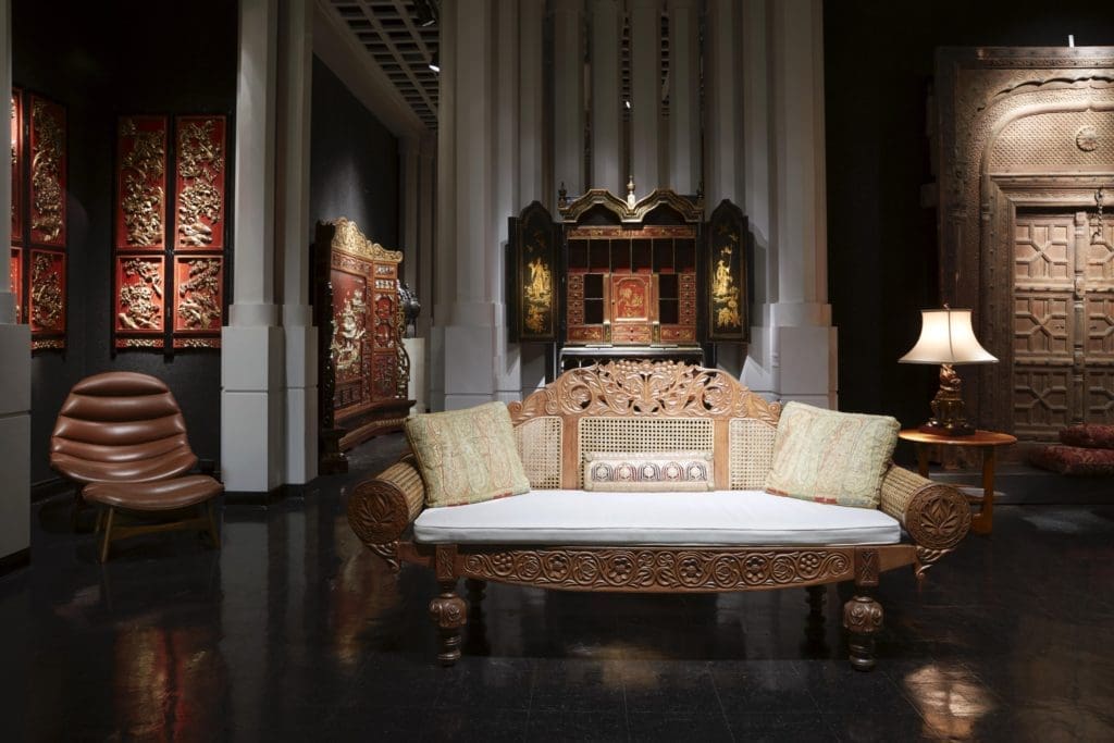 A British Colonial satinwood and cane settee, ornately carved with scrolling foliage, vines, and flowers. An English chinoiserie secretary from the early 20th century has gilt painted scenes of Chinese figures, pagodas, and gardens. (Photo by Pär Bengtsson)