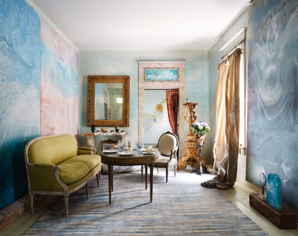 A pink-and-blue painting by Salle Werner-Vaughn, left, inspired this room installation in Houston. The artist also created the painting and sculptures at right and painted the cloud scene above the doorway. A monumental antique gilt candlestick is used as a pedestal for a tiny sculpture. (Photo by Lisa Petrole, Art Direction by Michelle Aviña)