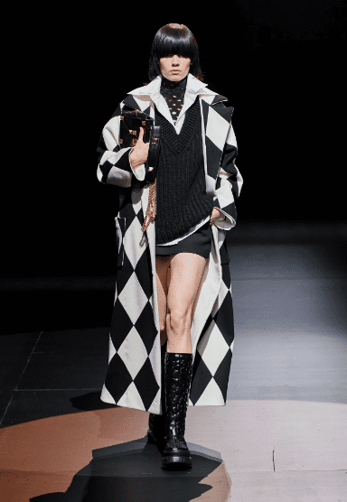 Valentino harlequin coat, black V-neck sweater and skirt, white shirt, laser cut turtleneck, embossed crocodile combat boots. (Photo courtesy of Valentino)