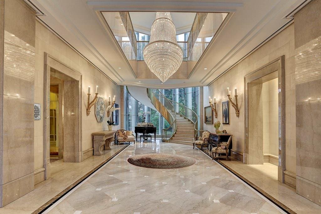 The dramatic floating staircase is the focal point of this spectacular foyer. The stunning marble treads and dual polished-brass balustrades float beautifully within an alcove of 35’ tall butted-glass windows,  (Photo by TK Images)