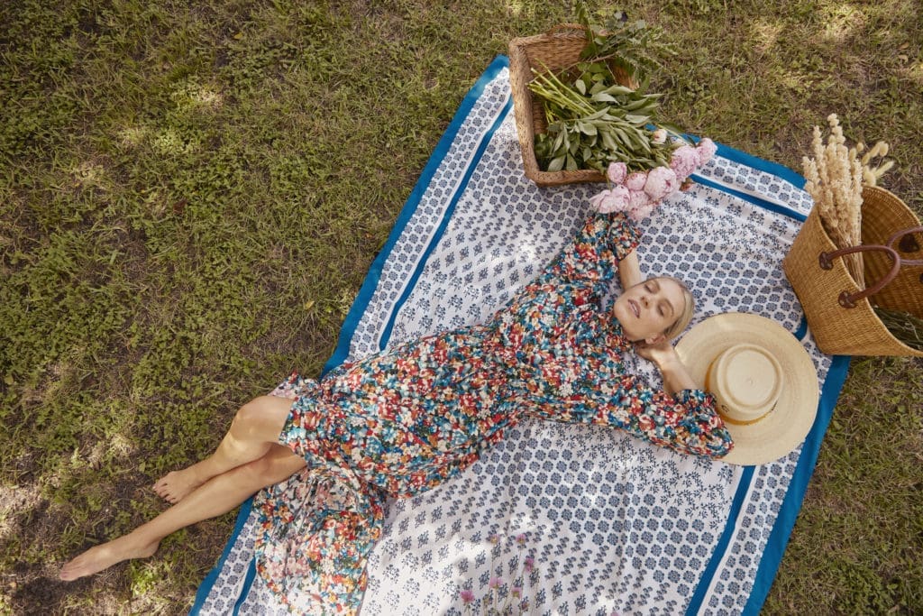 The model in Hunter Bell's Oakley in Wild Rose dress relaxes on the Western Willow Blue tablecloth, displaying its multiple uses.