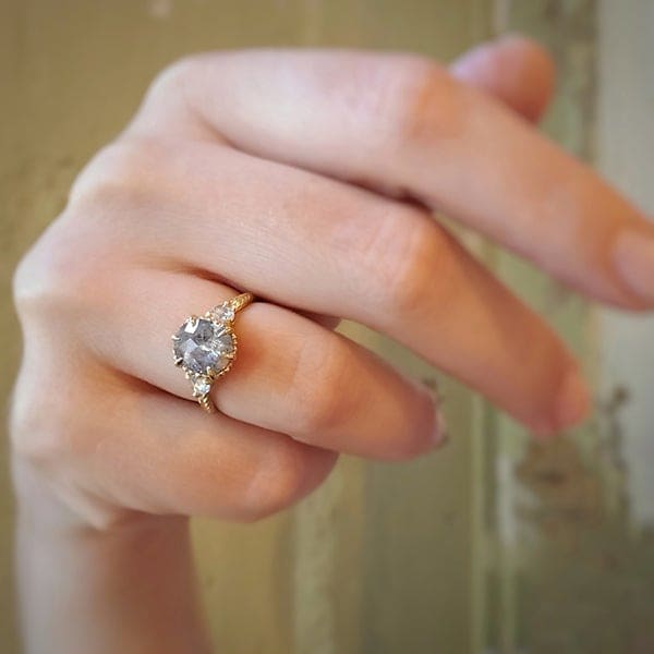 Megan Thorne's Evergreen Three Stone engagement ring is sided by two white rose cut diamonds. The salt and pepper diamond in the center weighs in at 2.02-carats. 