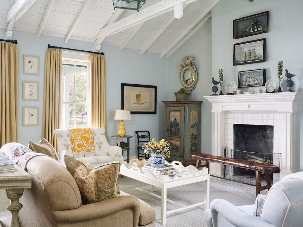 A seating area facing the fireplace in Rose Cottage with pale blues and soft yellows, painted furniture, and a striped rug. (Photo by Tria Giovan)