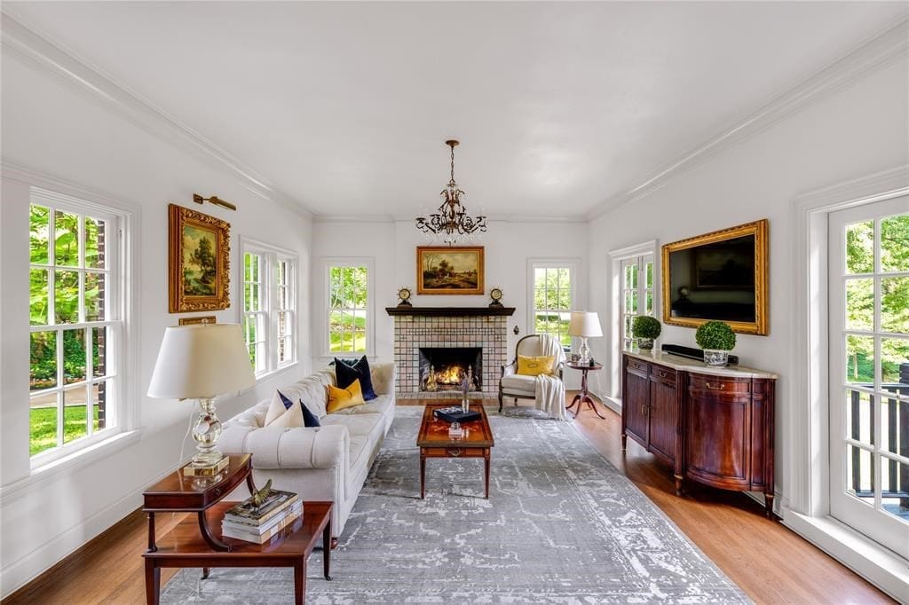 A window-lined formal living features an elegant (and highly valuable) Rookwood tile fireplace.