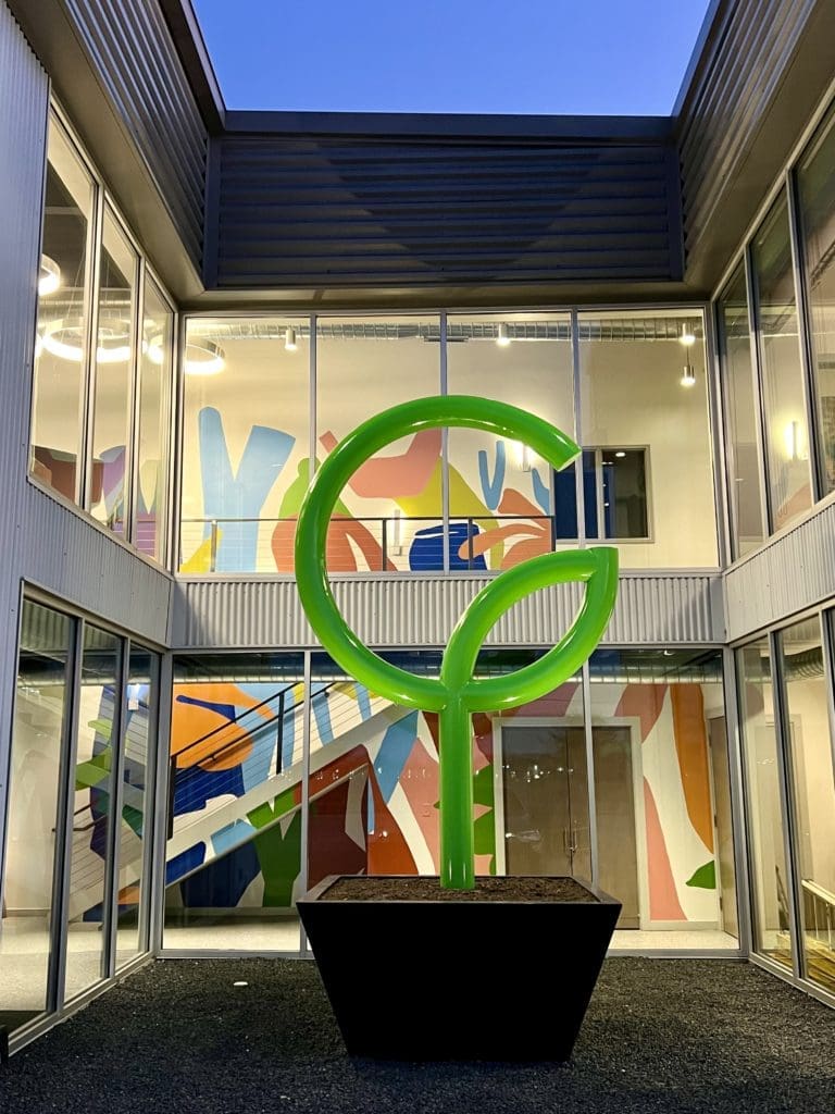 Shelbi Nicole's Good Earth mural provides a stunning backdrop to the sculpture of the company's logo. (Photo courtesy the artist.)