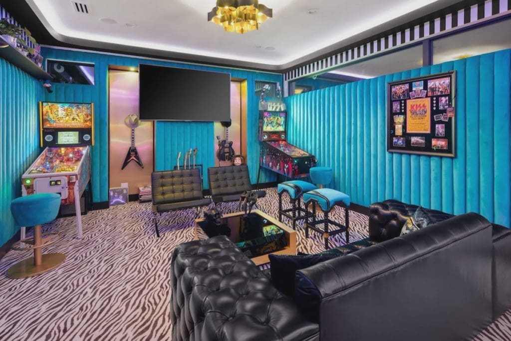 A game room and bar features tufted turquoise walls and custom-built pinball machines. 