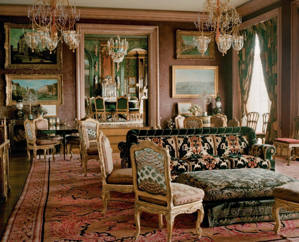 The music room, adjacent to the dining room, has a Russian theme that resonates with the English country overview of the house. The hand-knotted wool rug is Russian, formerly in the collection of the Scottish Duke of Hamilton, who used it when he took over the Queen's Apartments at the Palace of Holy Roodhouse in Edinburgh in 1684. Patchwork curtains from the estate sale of dancer Rudolf Nureyev's Paris apartment. (Photography by Lisa Romerein)