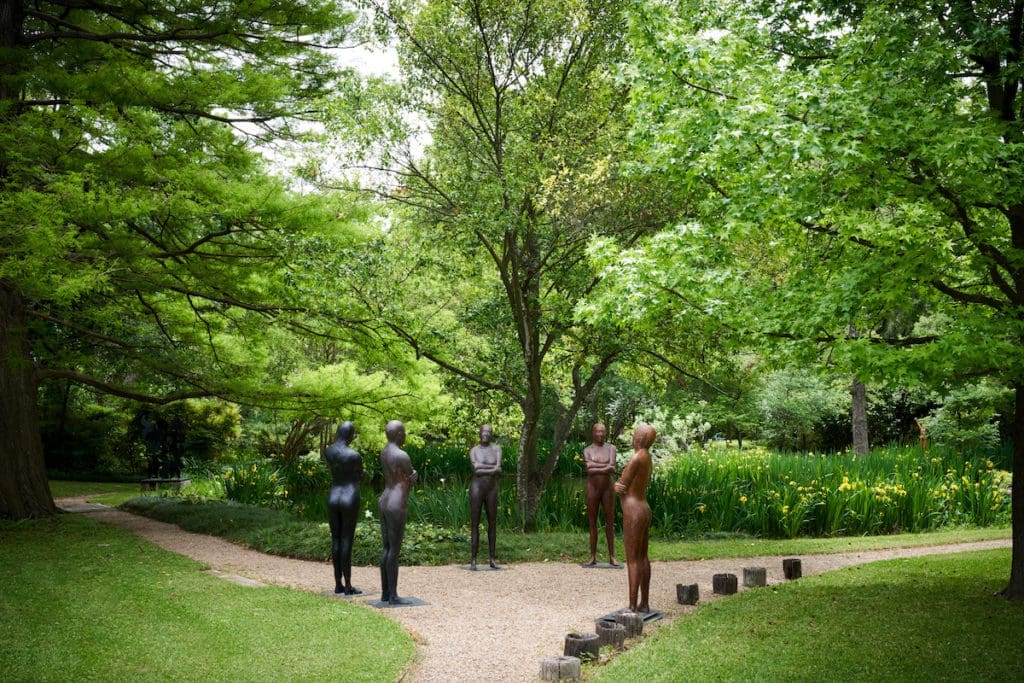 The four-acre garden at Cheryl and Kevin Vogel’s family home, Valley House, is dotted with sculptures including figurative pieces by Dallas artist Deborah Ballard. Small tree stumps along the gravel path are from the original garden designed by Clarence Roy in the late 1950s. (Photo by Pär Bengtsson / art direction by Michelle Aviña)