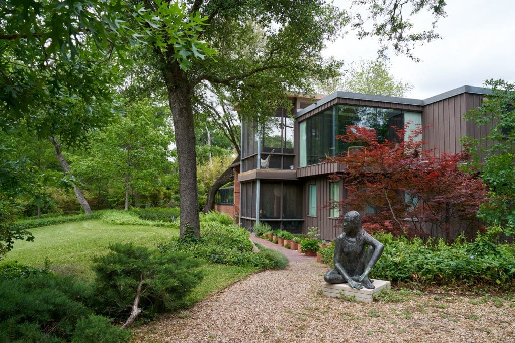 The storied Valley House sculpture garden in Dallas, shows Kevin's corner office and screened-in porches on both levels. Deborah Ballard sculpture, potted herb garden along the walkway. (Photo by Pär Bengtsson / art direction by Michelle Aviña)