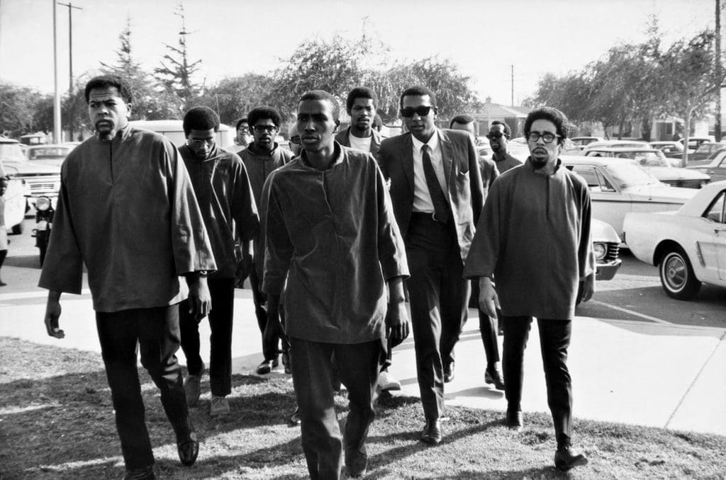 Gordon Parks' "Untitled, Watts, California," 1967. The photo shows members of the US Organization, including James Doss-Tayari (left), Tommy Jaquette-Mfikiri (behind Carmichael), and Ken Seaton-Msemaji (right), walking with Stokely Carmichael (pictured wearing a suit and sunglasses) to the Watts rally. (Courtesy The Gordon Parks Foundation)