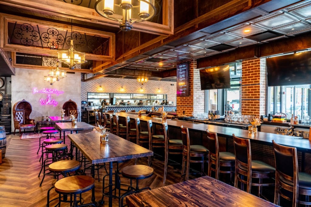 Inside the new Bosscat, the 5,000 square foot space with seating for 130 guests plays off the trend of industrial, rustic aesthetics–read: exposed brick, reclaimed wood, dark leather banquettes, and massive whiskey barrels all over the place. (Photo by Dylan McEwan)