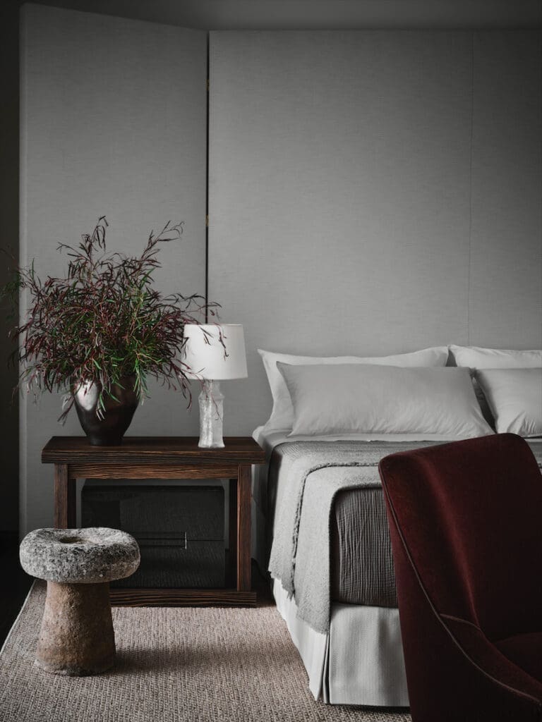 In the primary bedroom, a 10-foot- tall custom headboard upholstered in Perennials fabric. Society Limonta bedding, and an Edward Wormley slipper chair in plum mohair. (Photo by Douglas Friedman)