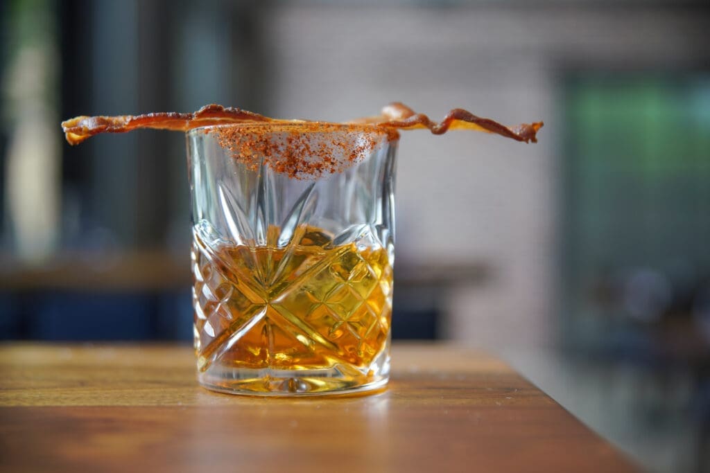 The Big Pig cocktail at Back Table. The signature Father's Day cocktail, crafted entirely in-house, features a blend of two ounce bacon-infused Bulleit bourbon, complemented by a smoky hint of agave smoked on cherry and oak wood and rimmed with their housemade BBQ rub. (Photo by Mario Santos)