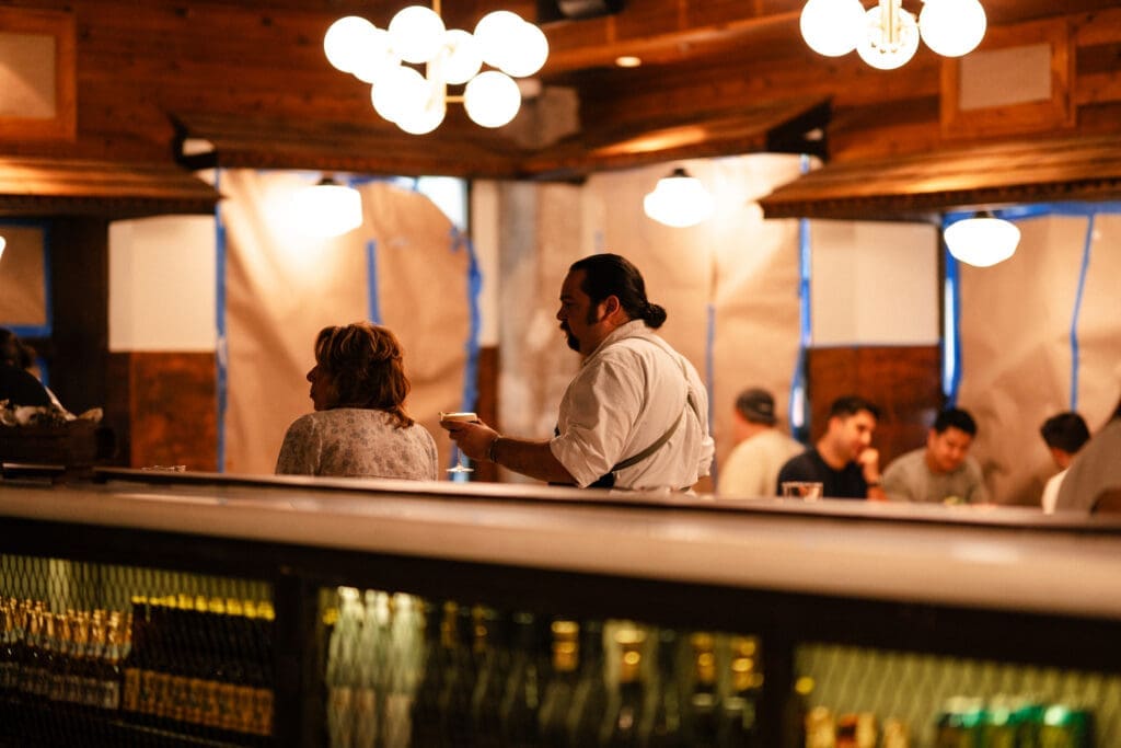 The dark reds and color-splashed murals inside have been replaced with rustic wood accents, painted tin ceilings, hex mosaic floors, and vintage light fixtures all fashioned by Nest Interiors. (Photo by  Ally Hardgrave )
