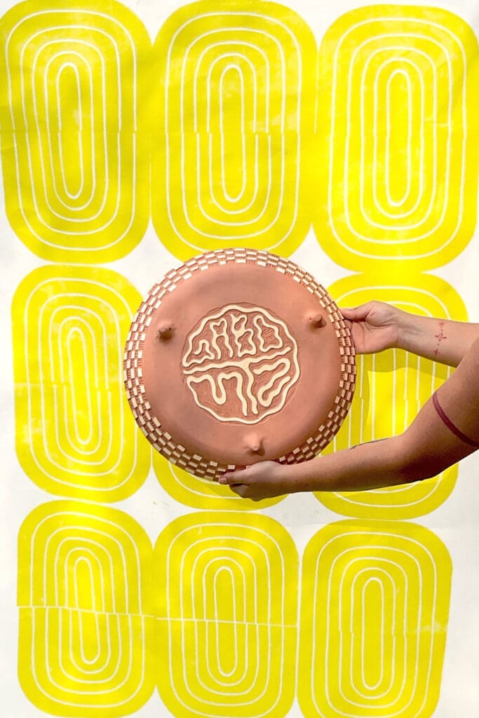 The bottom view of Gabo Martinez's  “Twelve Eyes Platter," 2023. Background: “Yellow Bloom Print,” 2021. On view at Houston Center for Contemporary Craft (Photo courtesy of the artist)