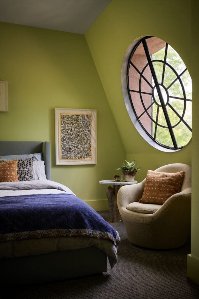 The round antique-glass window in Robert Bellamy’s bedroom slants inward like a garret apartment in Paris. Artwork by Ben Reynolds, Guatemalan coverlet from Garza Marfa. Side table made from a Japanese maple trunk.  (Photo by Pär Bengtsson)