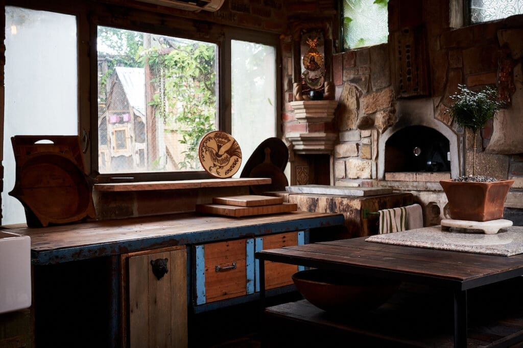 This kitchen with pizza oven was constructed from salvaged stone elements and is now enclosed. The chopping block is from a client’s former house, and the blue metal counter is repurposed from a shop on Riverfront. The salvaged window was reconfigured to prop open so he can serve guests. (Photo by Pär Bengtsson)