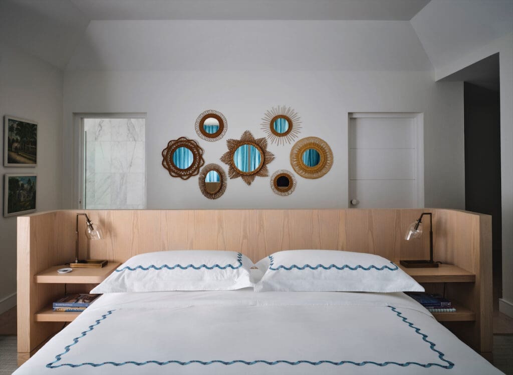 In a guest bedroom, a custom floating bed by Emily Summers Design Associates and Hamburg House linens. The collection of vintage rattan mirrors is from JF Chen, Los Angeles. (Photo by Douglas Friedman)