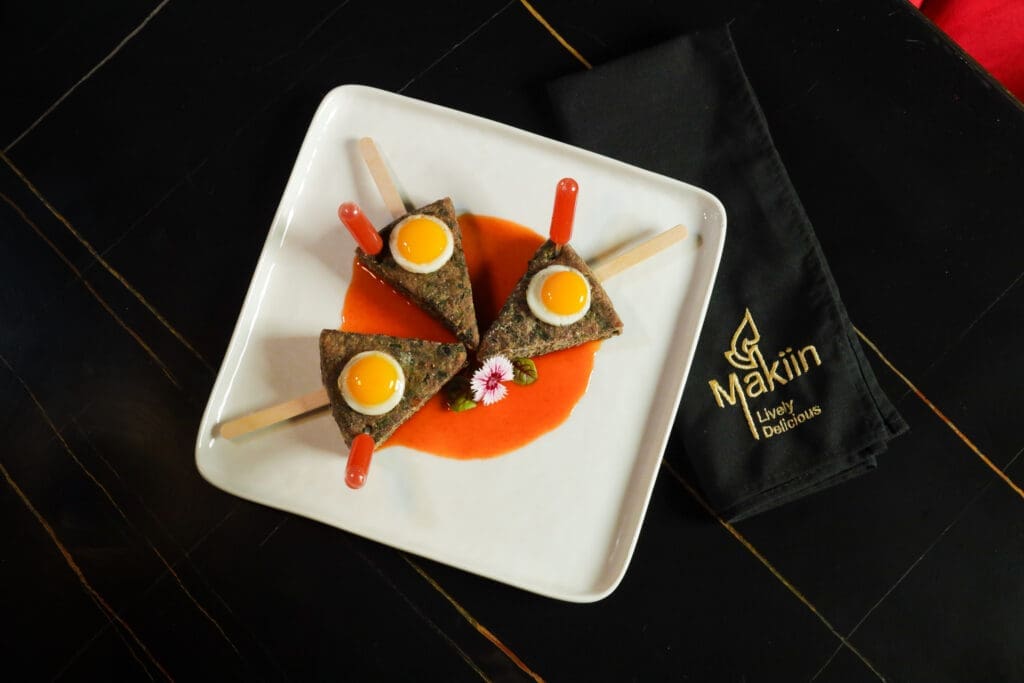 Chive Cake Sunrise at MaKiin is a rice-based dish that’s steamed and then pan-fried, made with chopped fresh chives that are baked on a stick, topped with a sunny-side-up quail egg and a squeeze of sweet Sriracha chili sauce. (Photo by Raydon Creative)