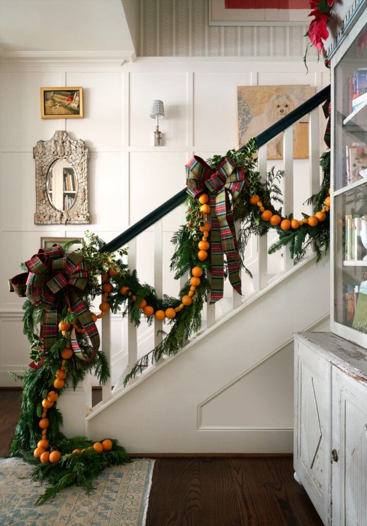 A staircase in the foyer of Cathy Kincaid’s cottage is draped with old-fashioned garlands of pine branches, mini tangerines, and kumquats handmade by Margaret Ryder of Kane & Co. (Photo by Pär Bengtsson)