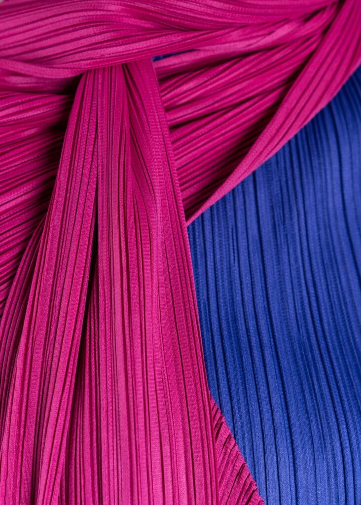 Close up of Issey Miyake's blue polyester pleated turtleneck top, Fall 1992, with pink polyester pleated coat and scarf, Fall 2004 (Photo by Shane Quereshi)