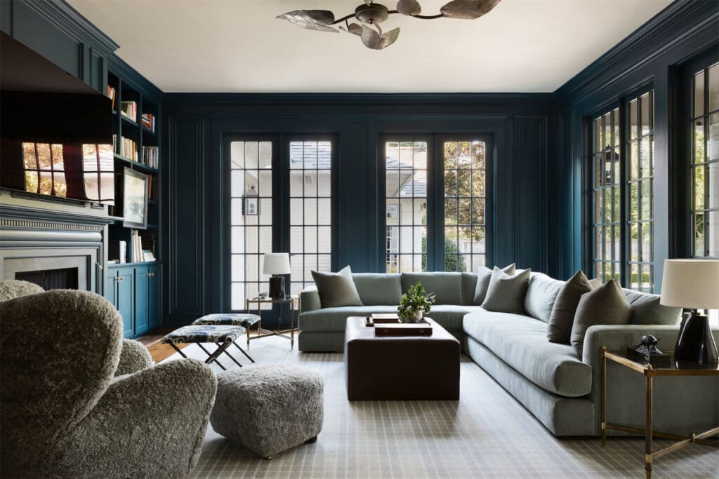 The family room is painted Farrow & Ball Hague Blue. Brass 1970s ceiling lamp from 1stdibs. Maiden Home sectional. Maison Jansen brass side tables. Audo sheepskin lounge chair and footstool from Copenhagen. Vintage 1960s brass benches from 1stdibs. Kim Salmela custom ottoman. Elan Atelier lamps from David Sutherland Showroom. Stark rug. (Photo by Trevor Parker)