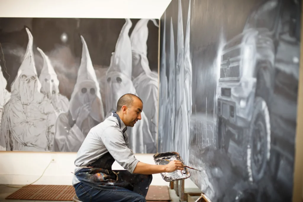Artist Vincent Valdez works on an eight-panel painting of modern-day Klansmen in his studio in San Antonio. (Photo by Michael Stravato)
