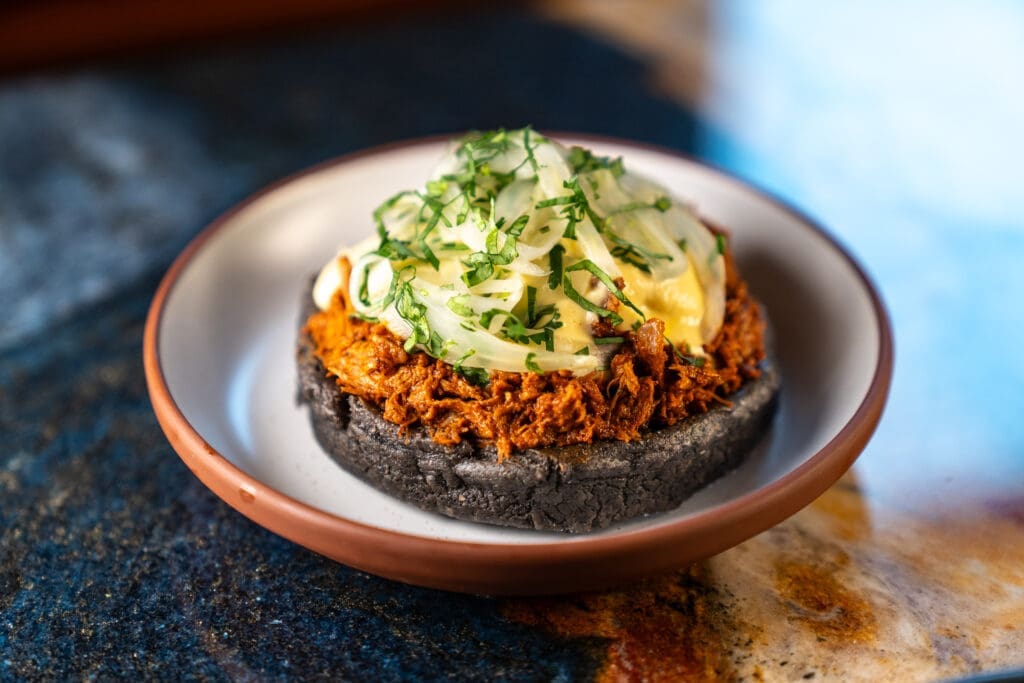 The cochinita pibil sope ($15) at the revamping Maximo is beautifully built upon a soft fried masa base and filled with shredded roasted pork shoulder with black beans, all crowned with a nest of finely shredded pickled fennel. (Photo by Carla Gomez)