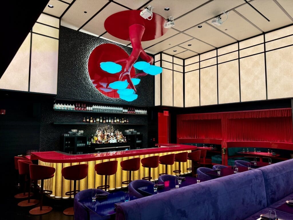 Japanese for “Dear Sir or Madam”(albeit with an extra “i” added), the dining room features an eight-foot-tall inverted bonsai tree glowing with LED embedded leaves that can change color at whim, each reflected in the red-tinted spherical mirror behind it framed with black river stones. (Photo by Photos by Karter Kendrick)